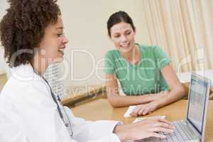 Doctor using laptop with woman in doctor's office smiling