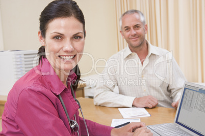 Doctor with laptop and man in doctor's office smiling