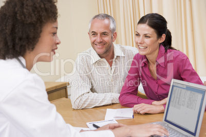 Doctor with laptop and couple in doctor's office smiling