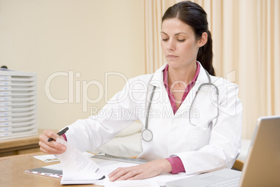Doctor with laptop writing in doctor's office smiling