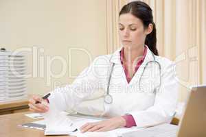 Doctor with laptop writing in doctor's office smiling