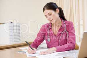 Doctor with laptop writing in doctor's office