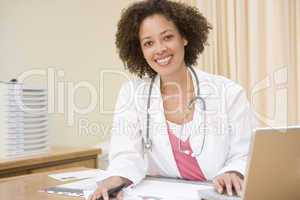 Doctor with laptop in doctor's office smiling