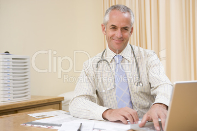 Doctor using laptop in doctor's office smiling