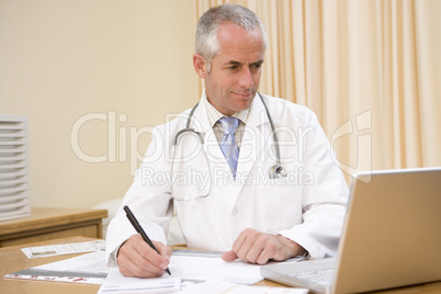 Doctor using laptop and writing in doctor's office