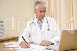 Doctor using laptop and writing in doctor's office