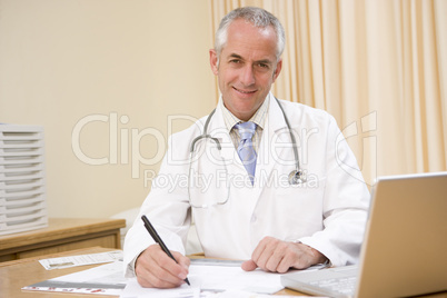 Doctor with laptop writing in doctor's office