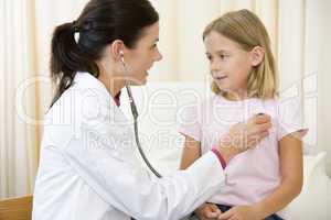 Doctor giving checkup with stethoscope to young girl in exam roo
