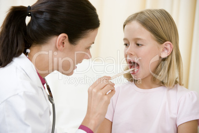 Doctor giving checkup to young girl with tongue depressor in exa