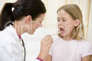Doctor giving checkup to young girl with tongue depressor in exa