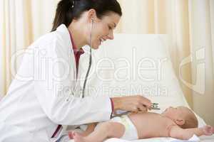 Doctor giving checkup with stethoscope to baby in exam room smil
