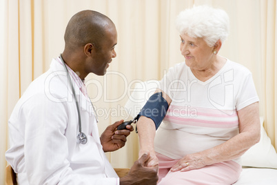 Doctor checking woman's blood pressure in exam room smiling