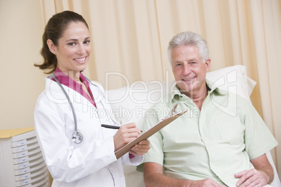 Doctor writing on clipboard while giving checkup to man in exam