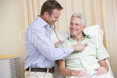 Doctor giving man checkup with stethoscope in exam room smiling