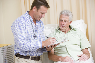 Doctor writing on clipboard while giving man checkup in exam roo