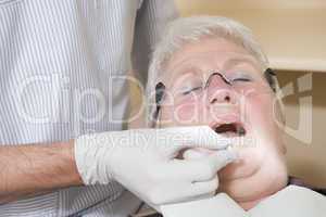 Dentist in exam room fitting dentures on woman in chair