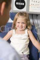 Optometrist in exam room with young girl in chair smiling