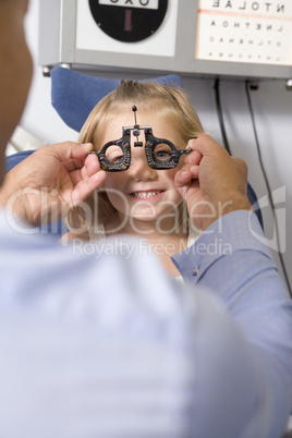 Optometrist in exam room with young girl in chair smiling