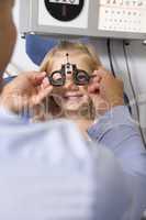 Optometrist in exam room with young girl in chair smiling