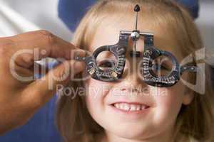 Optometrist in exam room with young girl in chair smiling