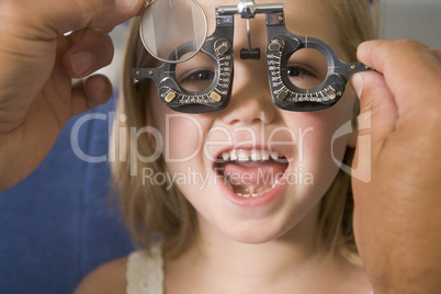 Optometrist in exam room with young girl in chair smiling