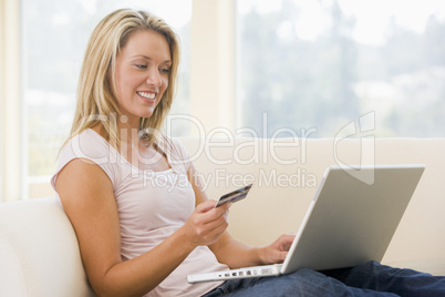 Woman in living room using laptop and holding credit card smilin