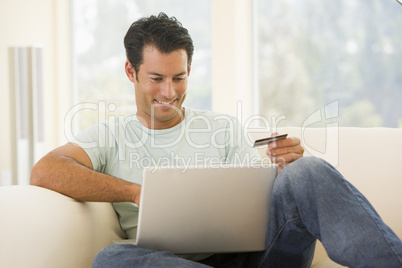 Man in living room using laptop and holding credit card smiling