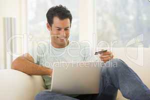 Man in living room using laptop and holding credit card smiling