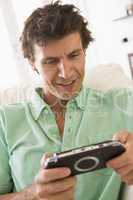 Man in living room playing handheld videogame smiling