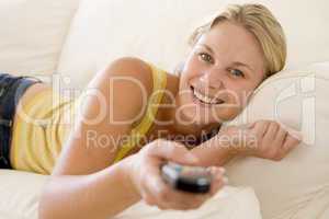 Woman in living room holding remote control smiling