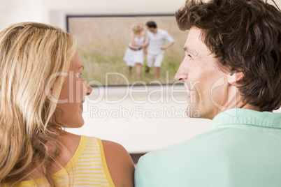 Couple in living room watching television smiling Couple in living room watching television smiling