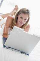 Woman lying in bed with laptop smiling