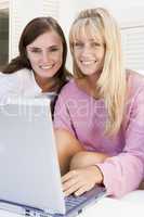 Two women on patio using laptop smiling