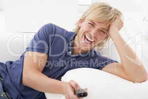 Man in living room holding remote control laughing