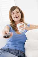 Woman in living room with remote control and coffee smiling