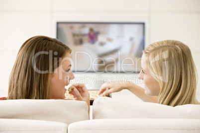 Two women in living room watching television eating chocolates s