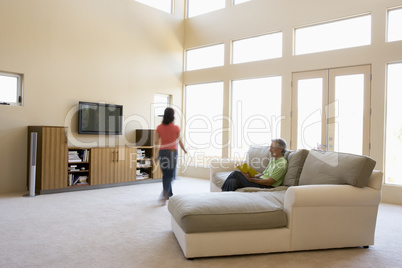 Man reading book in living room with woman walking by