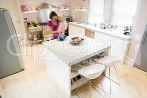Woman in kitchen whisking on counter holding baby