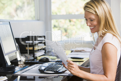 Woman in home office with computer and paperwork smiling