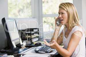 Woman in home office with computer using telephone frowning