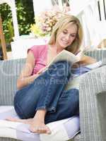 Woman sitting outdoors on patio with book smiling