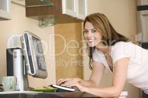 Woman in kitchen with computer smiling