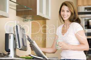 Woman in kitchen at computer with newspaper and coffee smiling