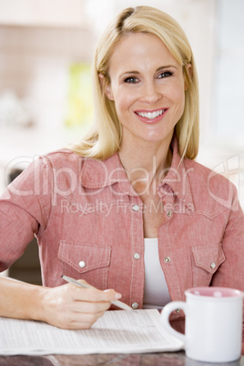 Woman in kitchen with newspaper and coffee smiling