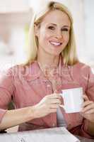 Woman in kitchen with newspaper and coffee smiling