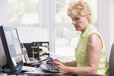 Woman in home office at computer with credit card frowning