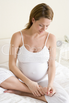 Pregnant woman sitting in bed rubbing feet