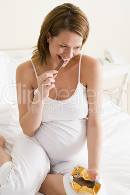 Pregnant woman in bed eating chocolate smiling