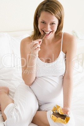 Pregnant woman in bed eating chocolate smiling