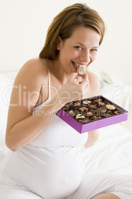 Pregnant woman in bed eating chocolate smiling